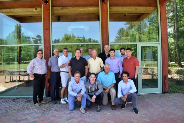 Group of men posing outdoors in front of a wooden building.